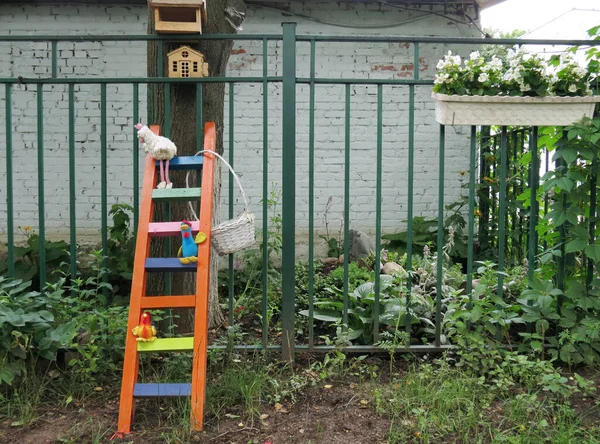 Garden decor - a wooden staircase with toy chickens, next to the garden there are white flowers on the fence