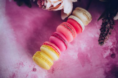 Satır kek macaroons parlak arka plan üzerinde. Üstten görünüm macaron tatlı kapatın. Pastel pembe, sarı renkler renkli badem çerezler. Vintage tarzı tonlama.