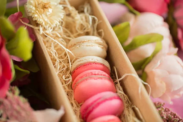 Row of cake macaroons in gift box on bright background. Close up macaron dessert on top view. Colorful almond cookies in pastel pink, yellow colors. Vintage style.