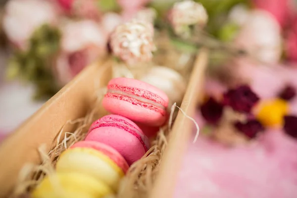 Row of cake macaroons in gift box on bright background. Close up macaron dessert on top view. Colorful almond cookies in pastel pink, yellow colors. Vintage style.