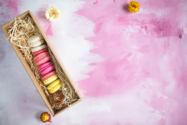 Row of cake macaroons in gift box on bright background. Close up macaron dessert on top view. Colorful almond cookies in pastel pink, yellow colors. Vintage style.