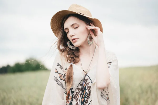 Girl in eco style clothes posing in nature background. Portrait of young woman in boho hat. Pretty ethno stranger in field.