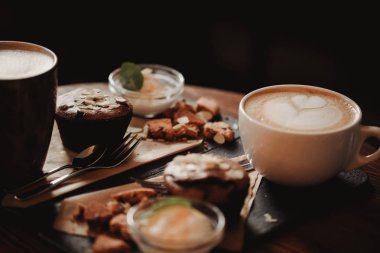 Fincan kahve ve tatlı ahşap masa arka planda Cafe gıda görüntüsünü kapatın. Eğilim sıcak tonlama. Küçük bir alan derinliği ile fotoğraf