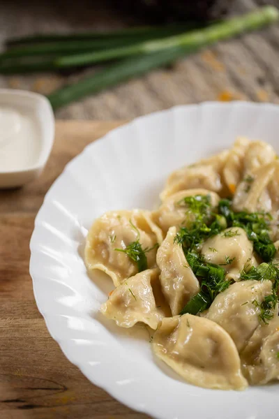 Russian National food. Close up view of traditional belorussian meal. Dumplings in white plate with green and sour. Food concept.