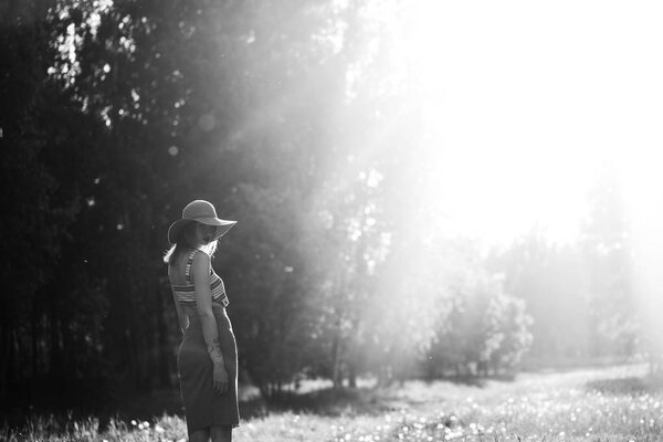 Silhouette of girl walking in park outdoor. Sunny summer lifestyle concept. Woman in dress and hat in field with dandelions. Light effect for text. Copyspace for design. BW photo