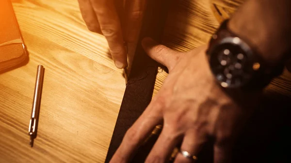 Working process of the leather belt in the leather workshop. Man holding tool. Tanner in old tannery. Wooden table background. Close up man arm. Warm Light for text and design. Web banner size.