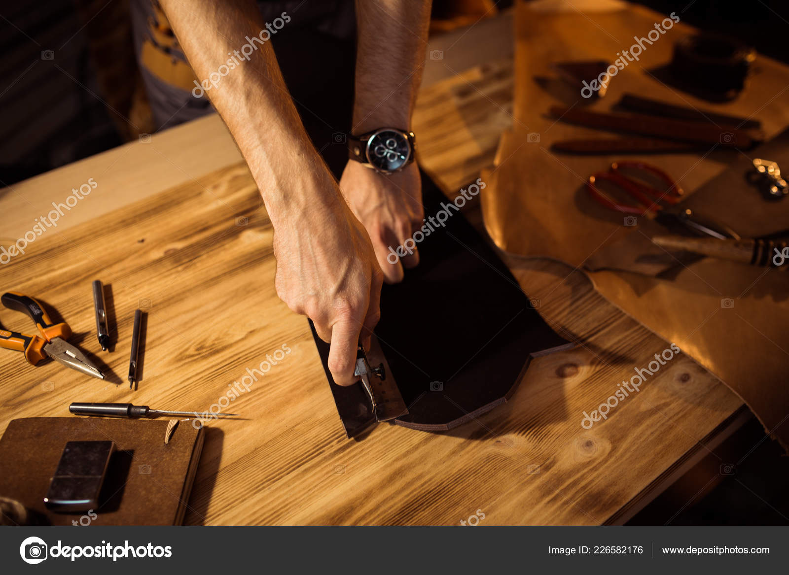Proceso de trabajo del cinturón de cuero en el taller de cuero. Hombre  sosteniendo herramienta de elaboración y trabajo. Tanner en curtiduría  vieja. Fondo de tabla de madera: fotografía de stock ©