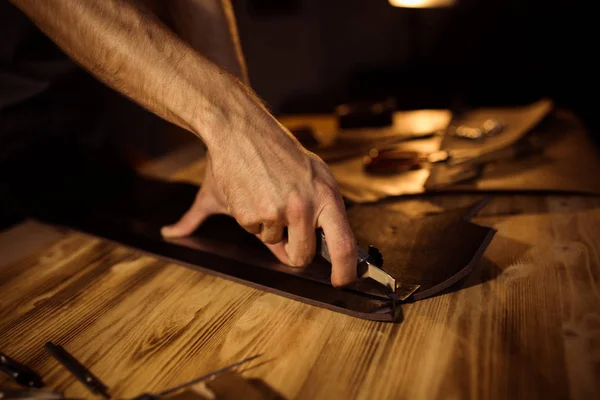 Processo di lavorazione della cintura in pelle nell'officina. Uomo in possesso di utensili artigianali e di lavoro. Abbronzatura nella vecchia conceria. Sfondo tavolo in legno — Foto Stock