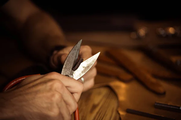 Arbeitsprozess des Ledergürtels in der Lederwerkstatt. Mann hält Werkzeug in der Hand und arbeitet. Gerber in der alten Gerberei. Holztischhintergrund. Nahaufnahme Mann Arm — Stockfoto
