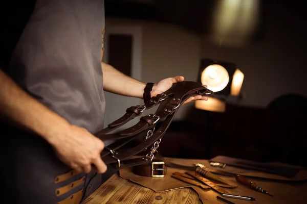 Processo di lavorazione della cintura in pelle nell'officina. Uomo in possesso di cintura fotografi per la fotocamera. Strumento su sfondo di legno. Abbronzatura nella vecchia conceria. Chiudi il braccio master — Foto Stock