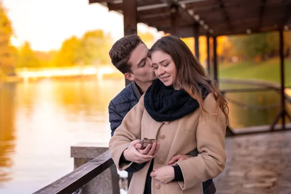 The guy makes a proposal to the girl. A young loving couple is standing in the autumn park with yellow trees. A man holds a box with a ring. Woman says yes.