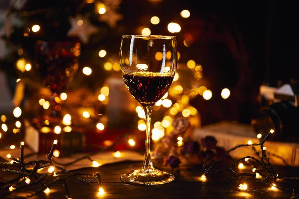 Ambiente festivo por la noche con una copa de vino tinto. Luz bokeh en el fondo. Navidad, Año Nuevo o San Valentín. Color dorado y enfoque suave — Foto de Stock