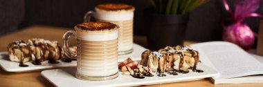 İki bardak pişmiş karamel kabuk ile sıcak latte boyutu görüntü afiş ve tatlı muz ve çilek ile kahve-dükkanda ahşap masa üzerinde rulo. Kahve kavramı.