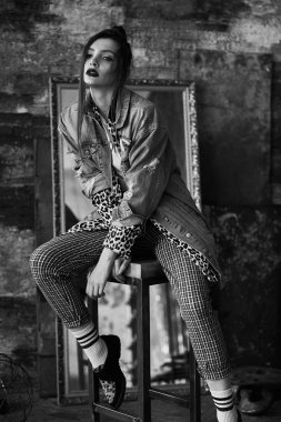 Grunge tarzında seksi bir kızın siyah-beyaz portresi. Karanlık bir arka plan üzerinde güzel bir kadının dramatik siyah beyaz fotoğraf. Denim ceket, ekose pantolon, beyaz çorap ve leopar ayakkabı kadın modeli