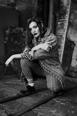 Grunge tarzında seksi bir kızın siyah-beyaz portresi. Karanlık bir arka plan üzerinde güzel bir kadının dramatik siyah beyaz fotoğraf. Denim ceket, ekose pantolon, beyaz çorap ve leopar ayakkabı kadın modeli
