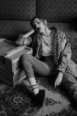 Grunge tarzında seksi bir kızın siyah-beyaz portresi. Karanlık bir arka plan üzerinde güzel bir kadının dramatik siyah beyaz fotoğraf. Denim ceket, ekose pantolon, beyaz çorap ve leopar ayakkabı kadın modeli