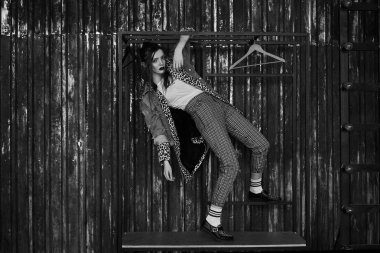 Grunge tarzında seksi bir kızın siyah-beyaz portresi. Karanlık bir arka plan üzerinde güzel bir kadının dramatik siyah beyaz fotoğraf. Denim ceket, ekose pantolon, beyaz çorap ve leopar ayakkabı kadın modeli