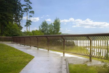 Metal çit boyunca parlak güneşli bir günde nehir kenarındaki yol. Güneş ışınları ile manzara