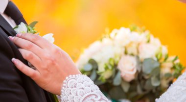 Gelin, damadın arka planında çiçek demeti olan bir kelebeğin elini tutuyor. Düğün günü..