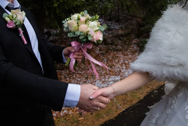 Groom gives a hand to the bride with a rear view of the bouquet and snow