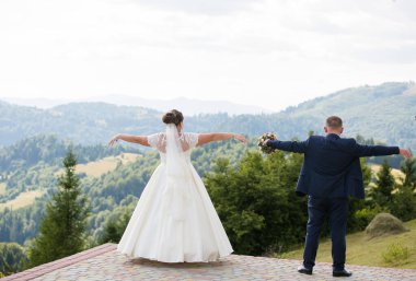 Dağın tepesinde gün batımlı bir gelinle damat.