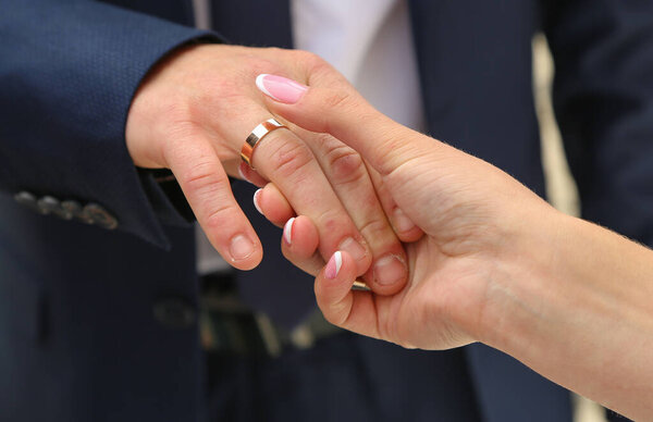 The bride holds the hand of the groom with a gold, engagement ring