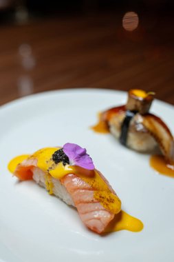 Ahşap bir masada beyaz bir tabakta yılan balığı ve somon balıklı suşi. Yan görünüm