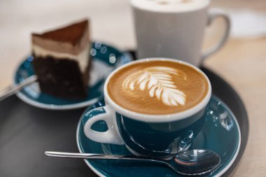 Bir fincan kapuçino ve masanın üzerinde bir parça kek.