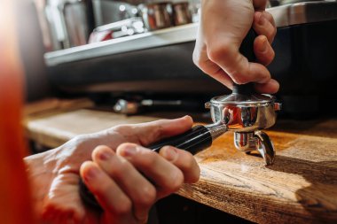 Barista kahve yapıyor, elinde bir iskele filtresi tutuyor ve kahveye bastırıyor. Yakın plan.