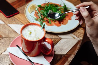 Bir fincan sıcak içecekle kafede bir kız. Eller ve kupa yakın çekim, yaşam tarzı