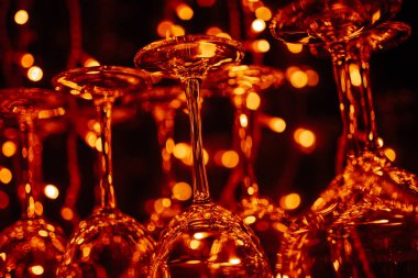 Boş temiz içki bardakları tezgahta asılı duruyor. Sıcak renkli, barın doğal ışığı.