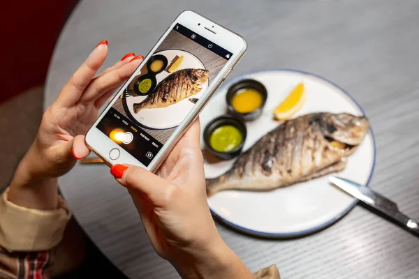 A woman photographs food on the phone in a restaurant. Close-up of hands