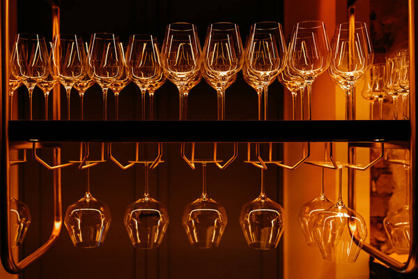 empty wine glasses stand in a row on a bar counter in orange lighting