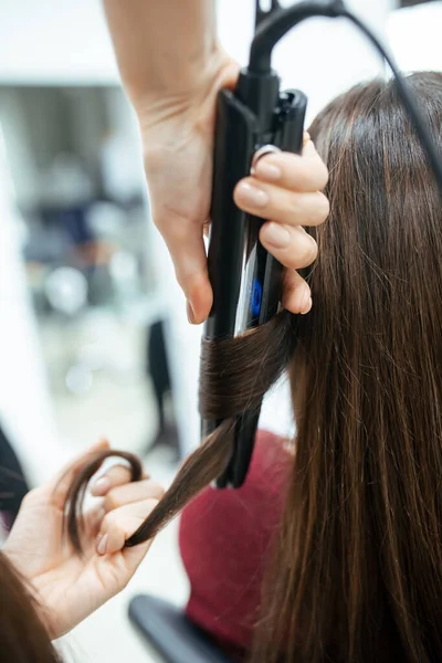 The work of a hairdresser. The master does styling hair and curling with tongs. Close-up of hands and tool