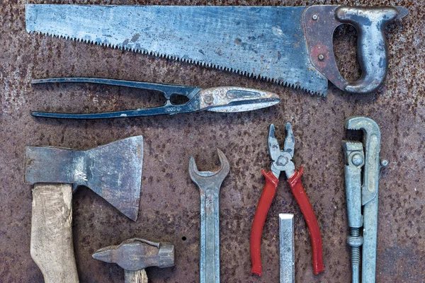 Set of old construction tools: hammer, saw, pliers, etc. on a flat lay background of rusty metal