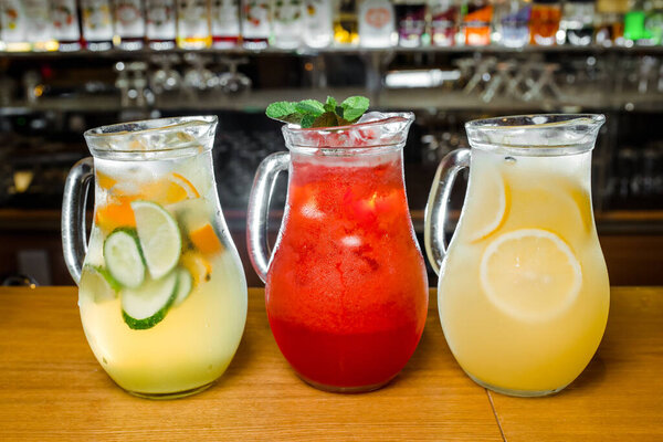 Three transparent jugs with refreshing cold red and yellow lemonade stand on a bar counter.