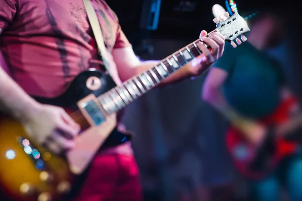 Müzisyen sahnede elektro gitar çalar. Gitar boynu, bir müzisyenin elinde rock müzik konseri için yakın çekim. Parmaklar panoda.