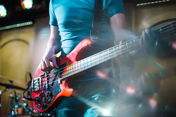 The musician plays the electric bass guitar on stage. Guitar neck close-up on a concert of rock music in the hands of a musician.  Fingers on fretboard. Guitar neck close-up on a concert of rock music in the hands of a musician.  Fingers on fretboard