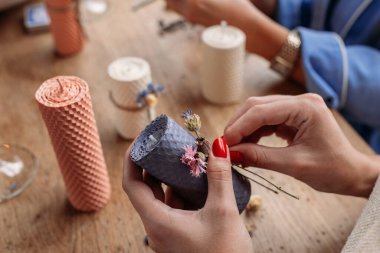 Balmumu yapma işlemi. Dekoratif mum yapan ve kurumuş çiçeklerle dekore eden bir kadın.