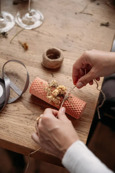 DIY wax candle making process. Woman making decorative wax candle and decorates with dried flowers, close-up of hands