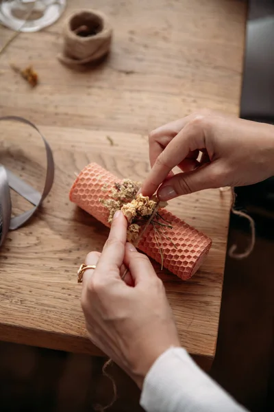 DIY wax candle making process. Woman making decorative wax candle and decorates with dried flowers, close-up of hands