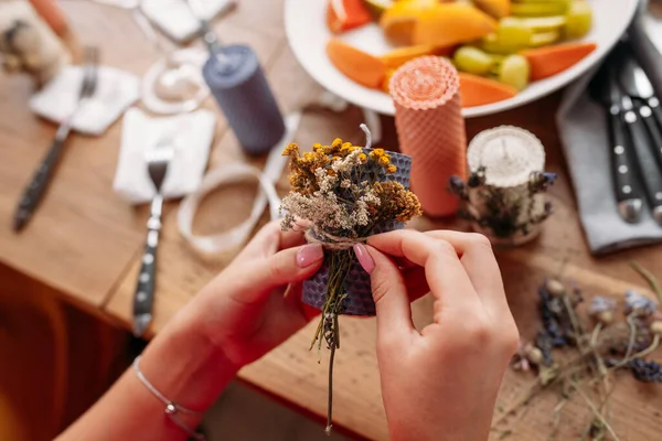 DIY wax candle making process. Woman making decorative wax candle and decorates with dried flowers, close-up of hands