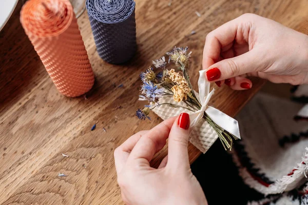 DIY wax candle making process. Woman making decorative wax candle and decorates with dried flowers, close-up of hands