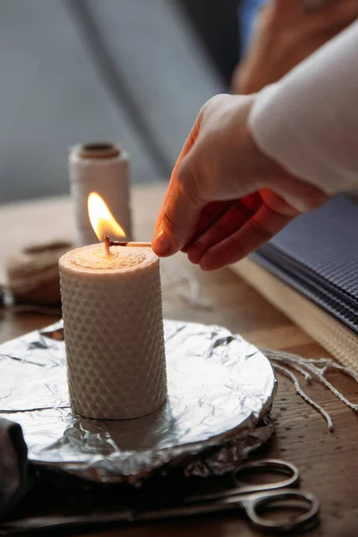 DIY wax candle making process. Woman lights decorative wax candle, close-up of hands