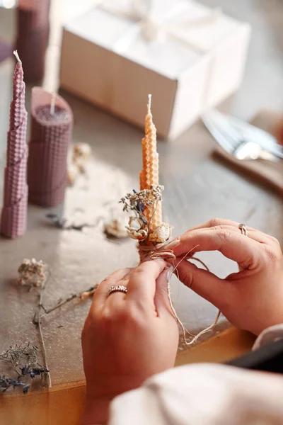 DIY wax candle making process. Woman making decorative wax candle and decorates with dried flowers, close-up of hands