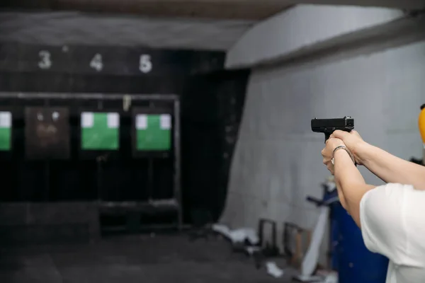 Shooting range. Rear view of woman shooting with gun in shooting range