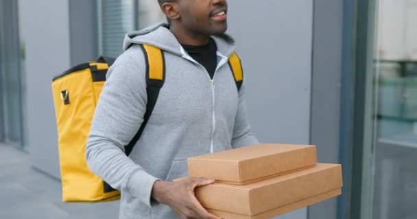 Afroamerikaner mit Päckchen, die während der Arbeit die Straße entlang laufen. Männlicher Kurier, der einen Spaziergang macht, um Kisten auszuliefern. Postangestellte spazieren im Freien. — Stockvideo