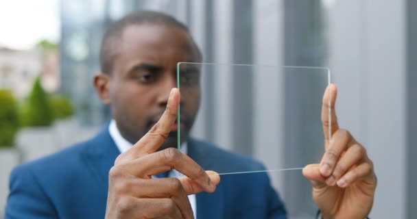 Primo piano di giovane uomo d'affari afro-americano in giacca e cravatta in piedi in strada e con lo schermo trasparente in vetro su cui guardare qualcosa come sullo schermo digitale. Dispositivo tecnologico futuro . — Video Stock