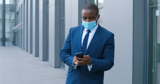 Hombre de negocios afroamericano en traje, máscara médica y corbata desinfectando el teléfono inteligente de gérmenes y llamadas. Hombre limpiando teléfono y desinfectando. Desinfección del teléfono celular antes de la llamada Hablando por teléfono — Vídeos de Stock