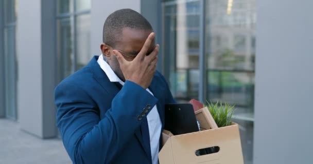 Africano americano irritado trabalhador de escritório masculino em depressão com caixa de coisas pessoais. O empresário perdeu o emprego. Homem despedido a andar ao ar livre. Deprimido sem emprego. Conceito de desemprego. Esquerda sem dinheiro . — Vídeo de Stock